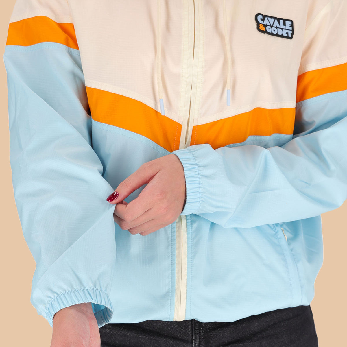 Veste coupe-vent Cavale & Godet à capuche, beige, orange et bleu.