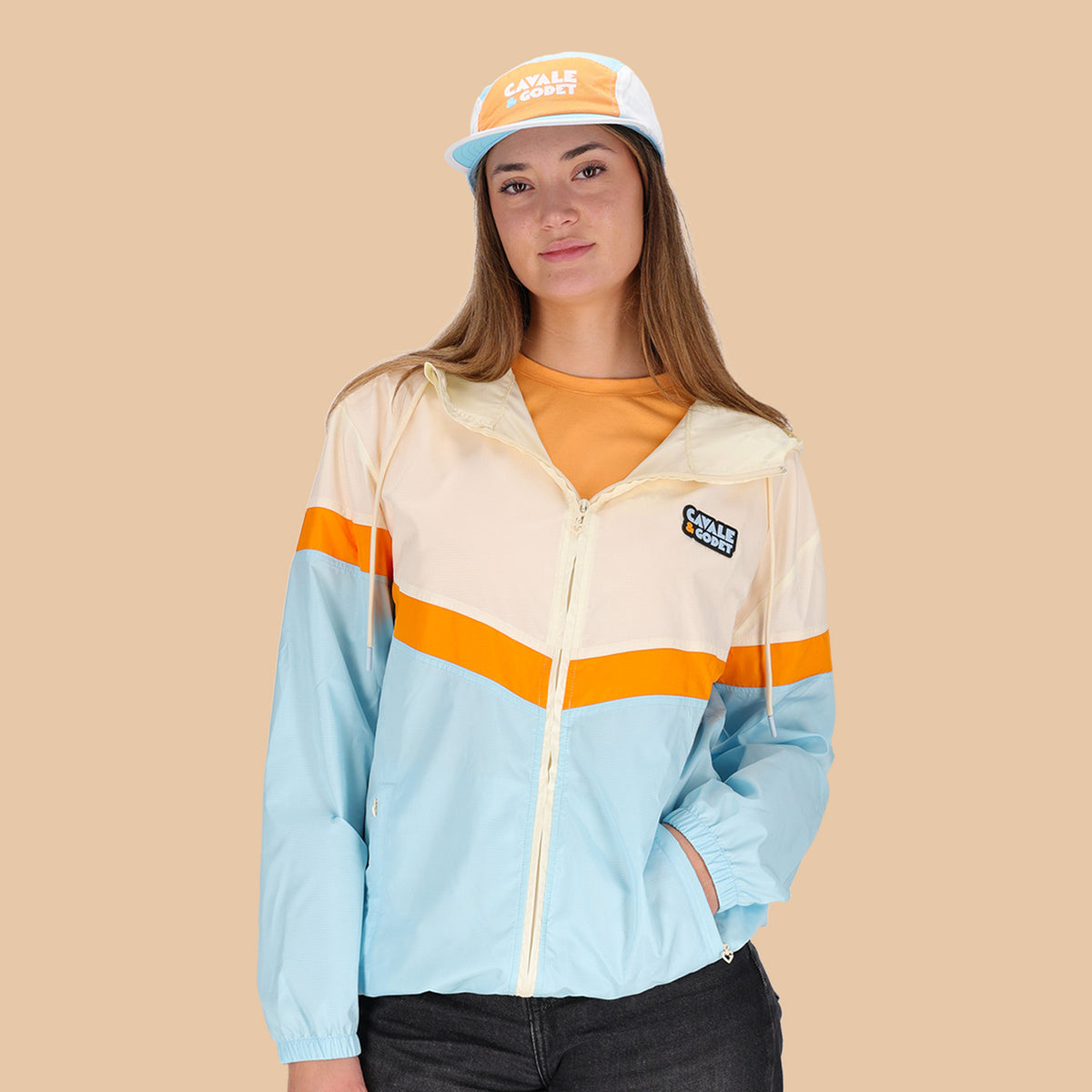 Veste coupe-vent Cavale & Godet à capuche, beige, orange et bleu.