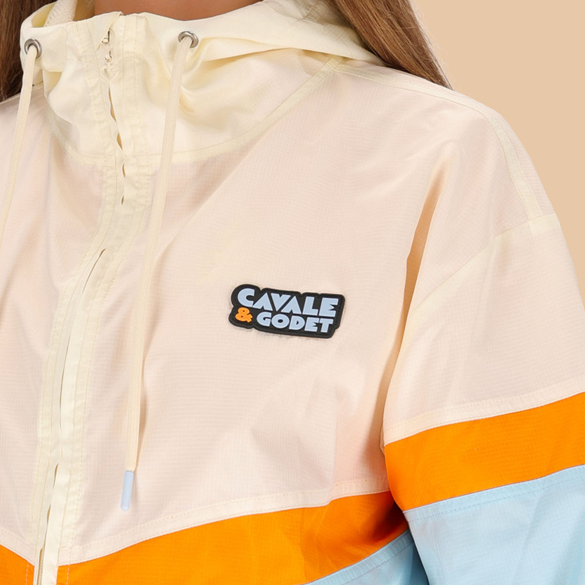 Veste coupe-vent Cavale & Godet à capuche, beige, orange et bleu.
